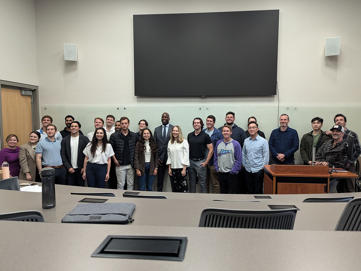 Photo: A group of about 25 students stand at the front of a lecture hall with speaker Malcolm Johnson