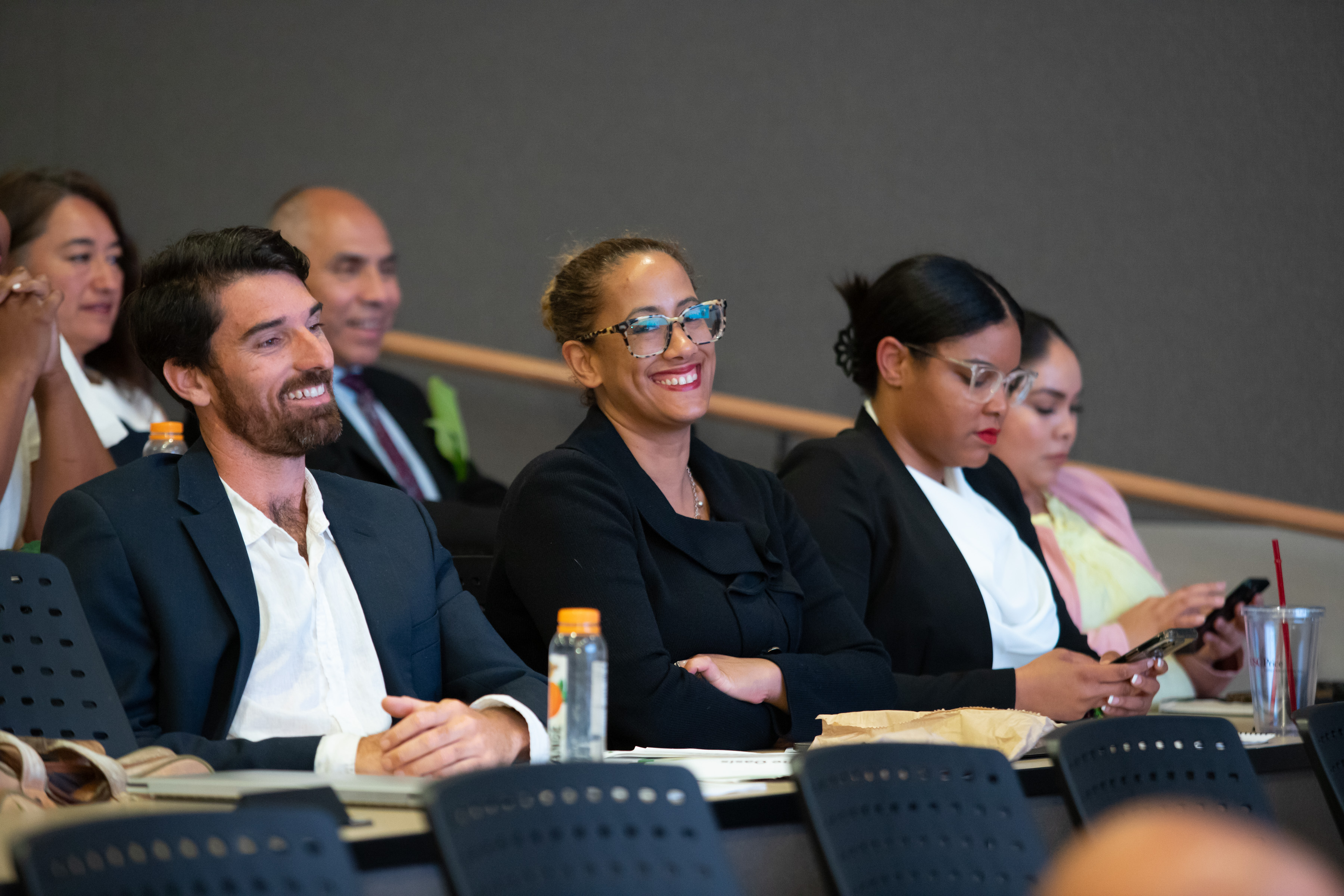 Photo: Six Ross participants seated in a lecture hall wearing business dress. Two are smiling.