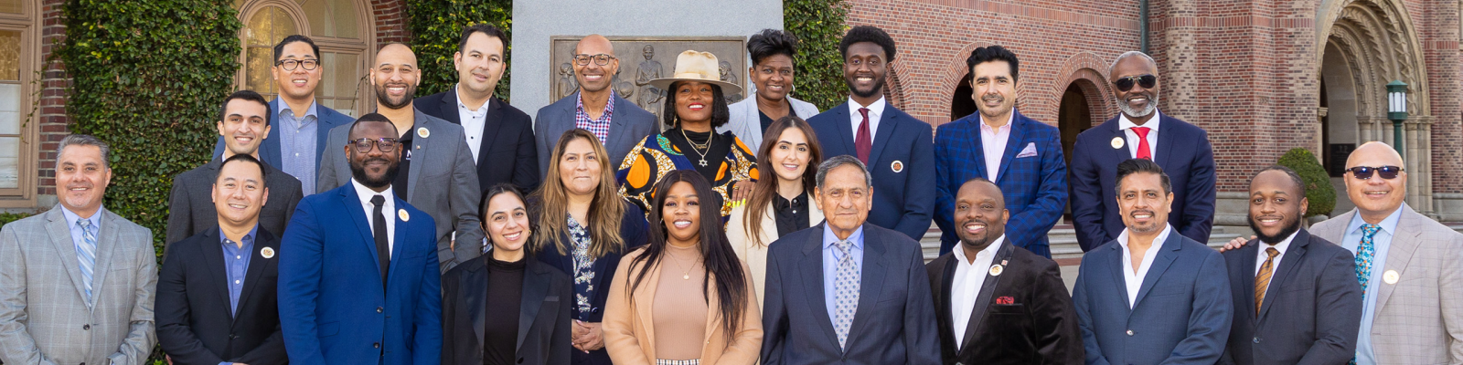 Photo: Ross Winter 2024 Session class. A group of about 25 people stand in front of the Tommy Trojan statue on USC campus. They are all wearing professional dress and comprise a diverse make up of genders and ethnicities including Black, Latino, Asian, White, and more. 